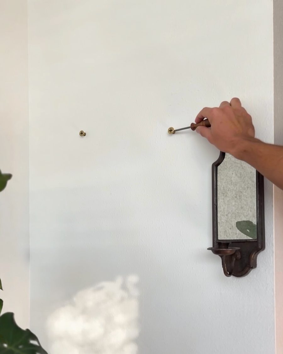 A hand driving two screws into the wall
