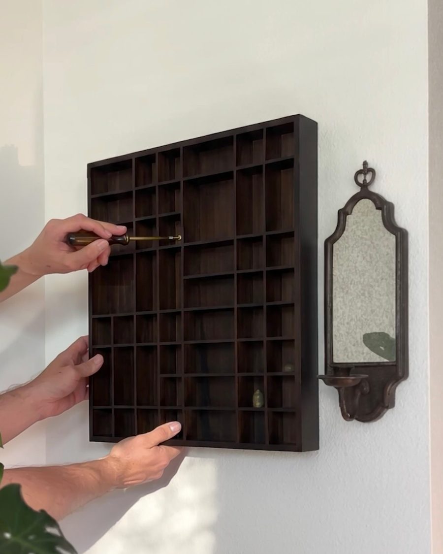 Hands holding the shelf to the wall and driving a screw
